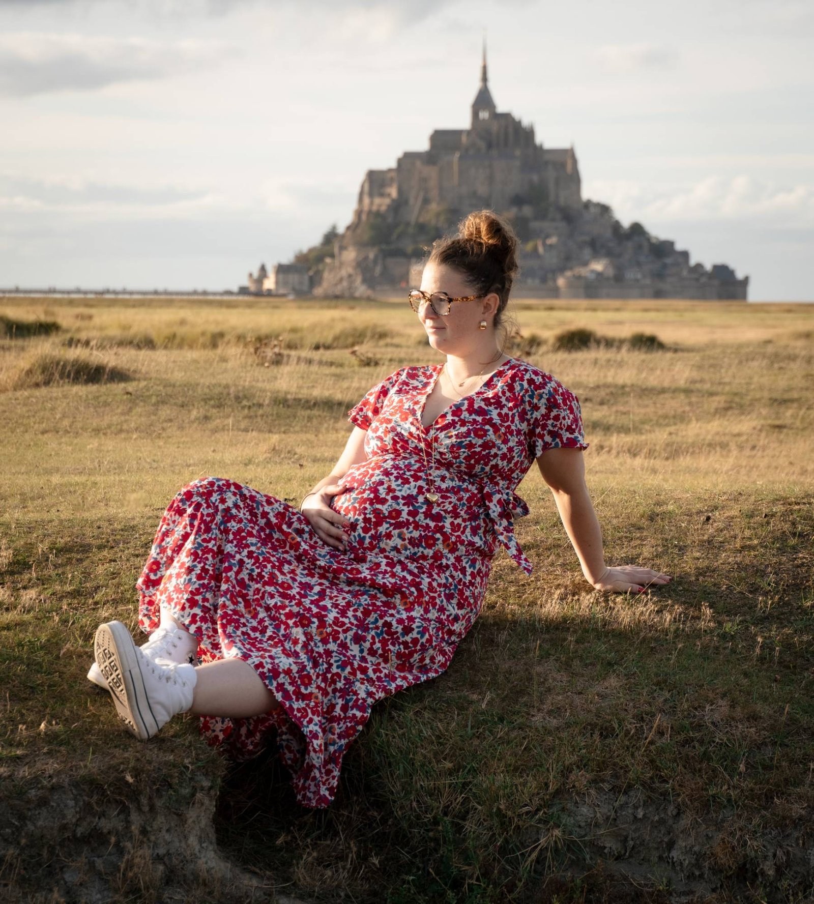 Future maman en robe fleurie assise face au Mont-Saint-Michel
